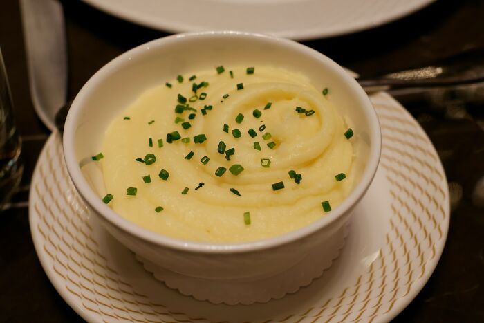 A bowl of mashed potatoes garnished with chives, a unique meal choice by a plane seatmate during a flight.