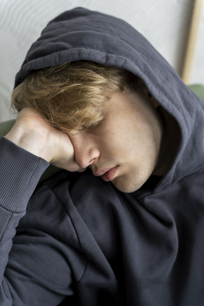 A young man in a dark hoodie rests his head on his hand, showing children dealing with unspoken struggles.