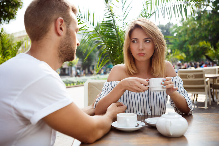 A woman looking skeptical at a man during coffee, illustrating the lies men tell.