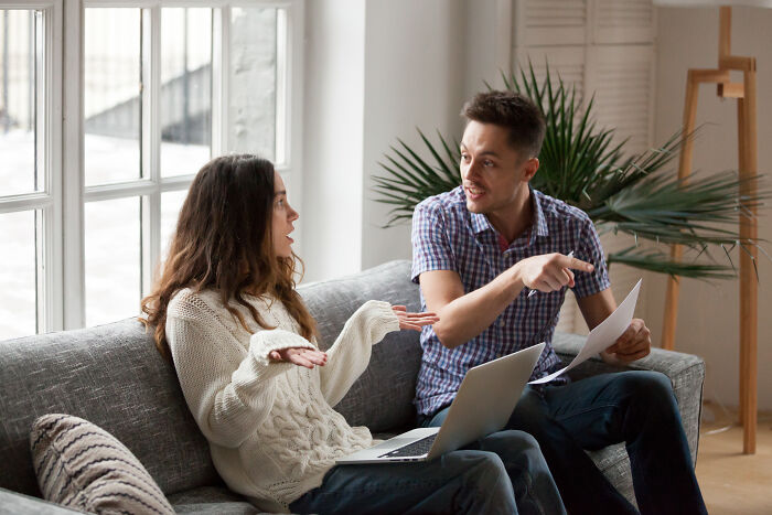 A man and a woman argue on a sofa, with the man pointing and holding papers, discussing their marriage before divorce.