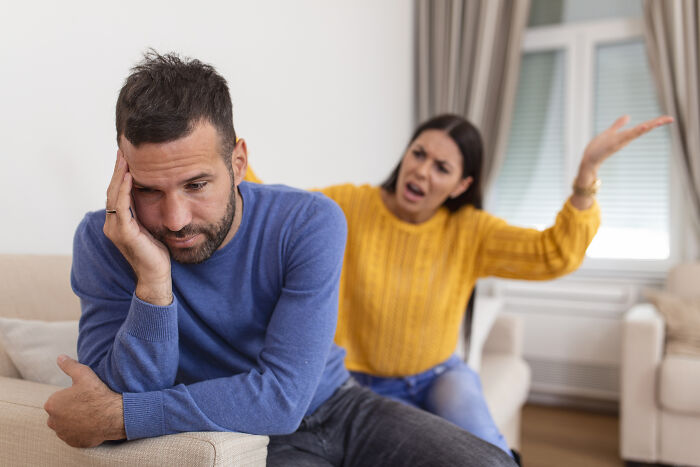 A sad man sitting on the couch while his partner yells at him, showing why their marriage couldn't be saved.