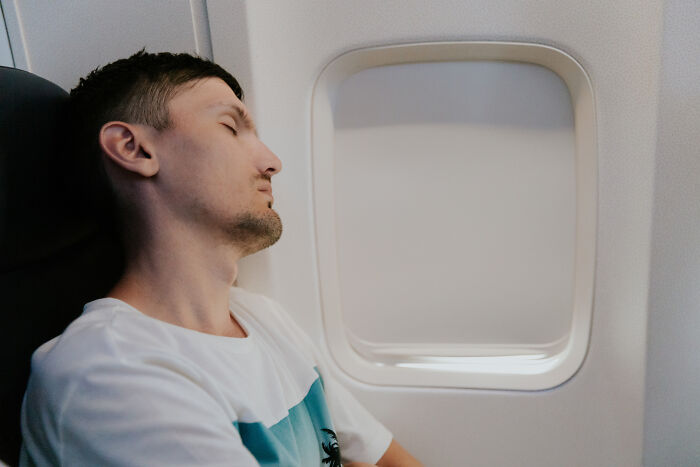 A man sleeping on an airplane, reflecting passenger behaviors that can be bothersome to flight attendants.