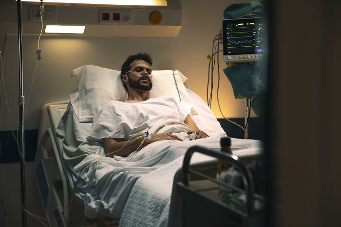 A man lies in a hospital bed with medical tubes and monitoring equipment, symbolizing extreme illness and sickness.