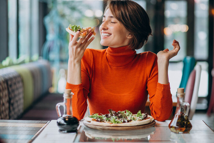 A happy woman enjoying a slice of pizza alone, showing life for divorced people can be peaceful.