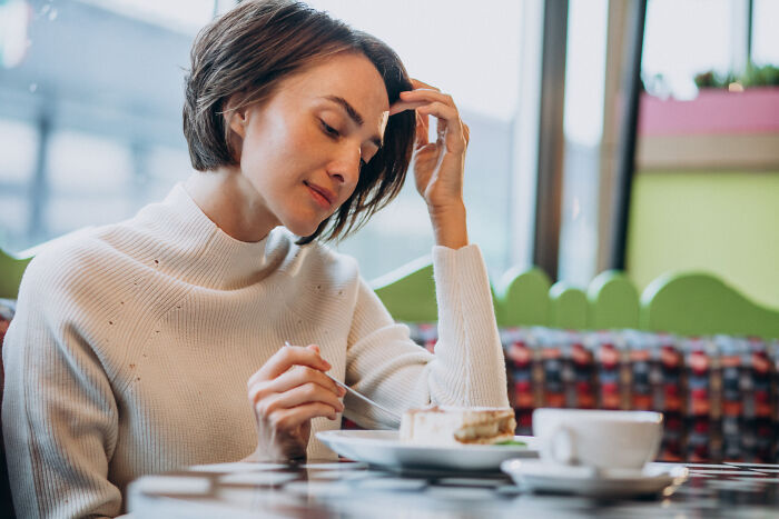 A woman on a first date looking sadly at her slice of cake and coffee, suggesting an awkward experience.