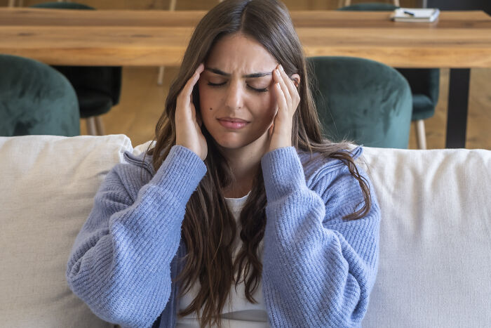 A woman holding her head in pain on a couch, highlighting the stress of subtle sexism