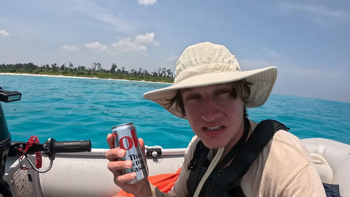 A YouTuber on a boat, holding a drink, approaching one of the most dangerous islands in the world.