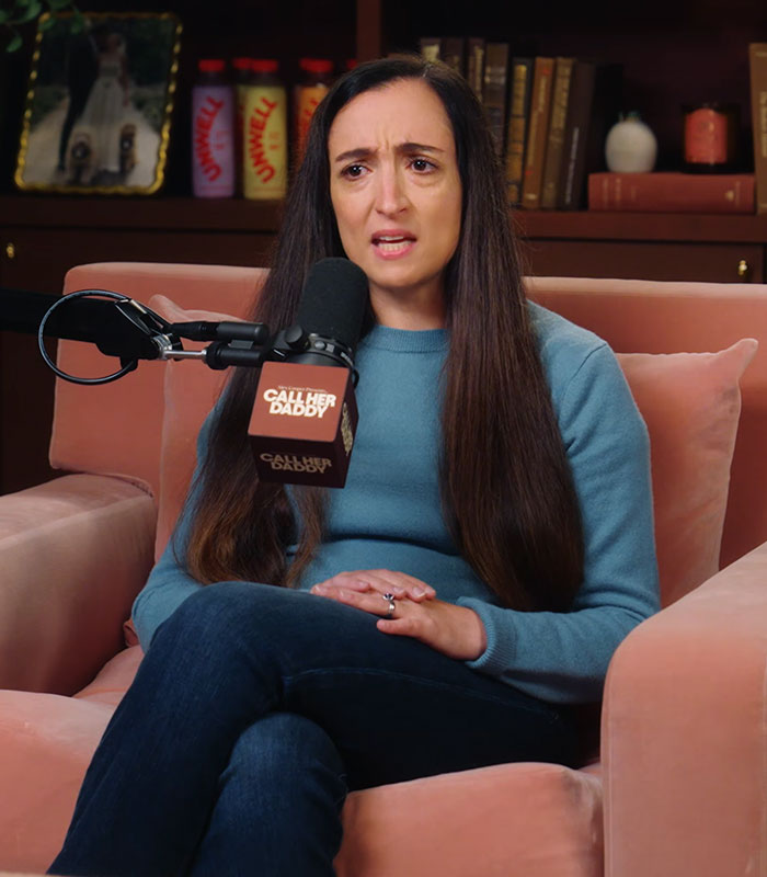 A woman sitting on a couch speaking into a microphone during a podcast about the Cornell 7 scandal.