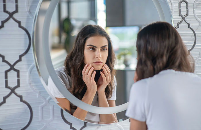 Woman examining skin in mirror concerned about white spots on skin