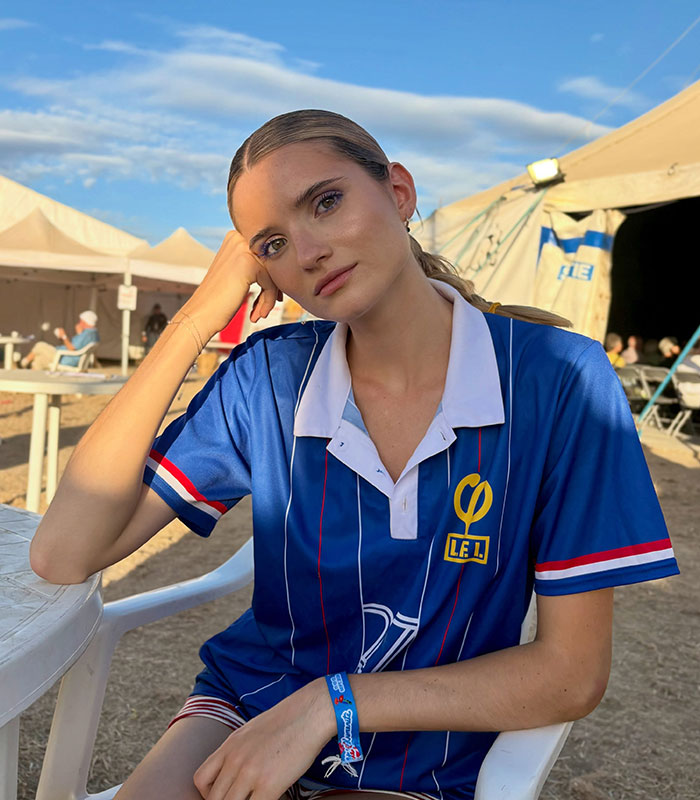 An influencer sitting at an outdoor table wearing a blue striped sports jersey with yellow branding