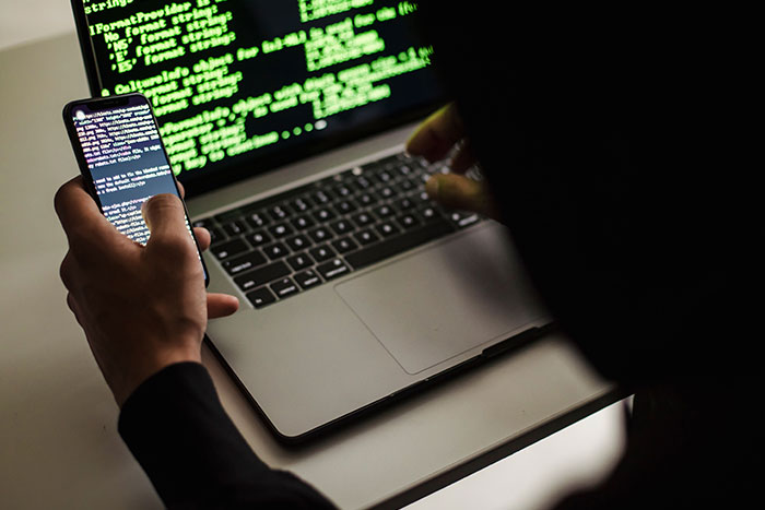 Hacker typing on laptop and phone with green code on screen related to AI agent swarms hacking internet. Hacker typing on laptop and phone with green code on screen related to AI agent swarms hacking internet.