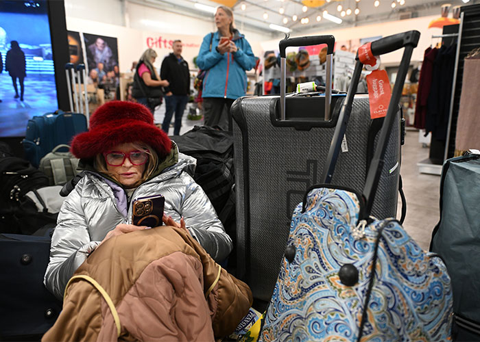 A woman sitting with piled luggage checks her smartphone while waiting for a permanent cruise departure.