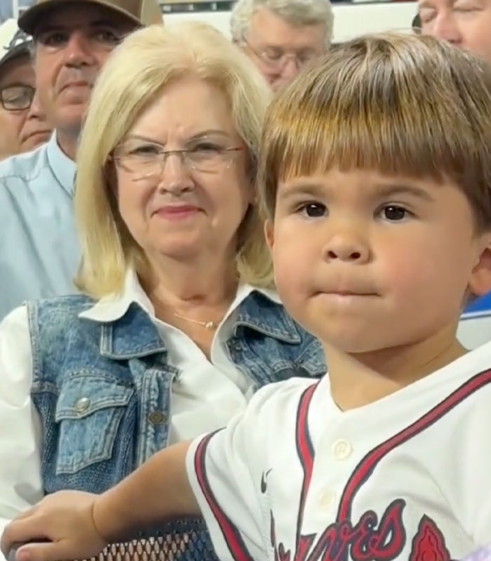 A young baseball fan sitting next to an older woman in the stands, looking forward.