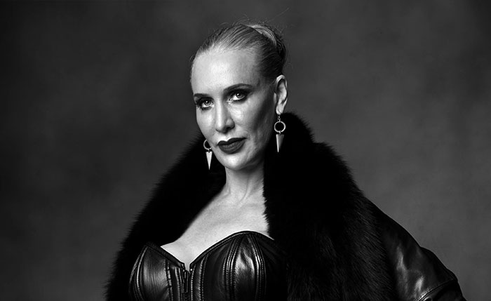 Black and white portrait of a 6 foot 5 tall Domme wearing a black fur coat and leather corset. Black and white portrait of a 6 foot 5 tall Domme wearing a black fur coat and leather corset.