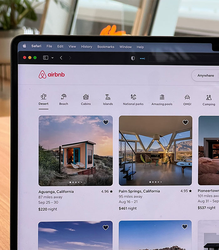 A laptop screen displaying the Airbnb host booking website with various vacation rental listings