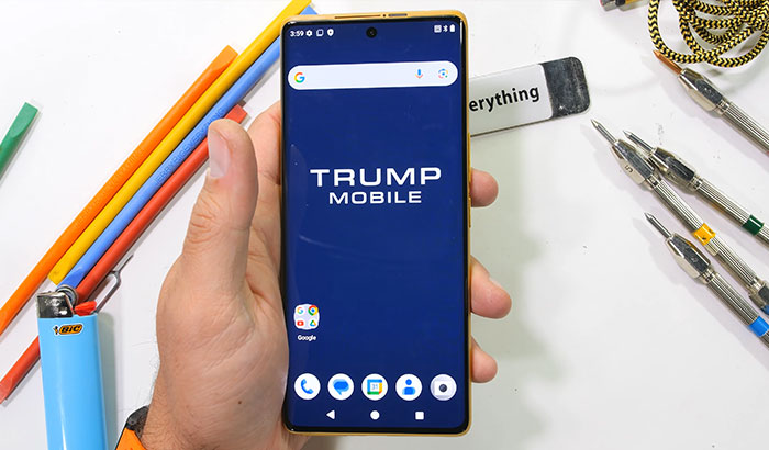 A tech reviewer holding the Trump Mobile 499 dollar phone displaying its home screen logo