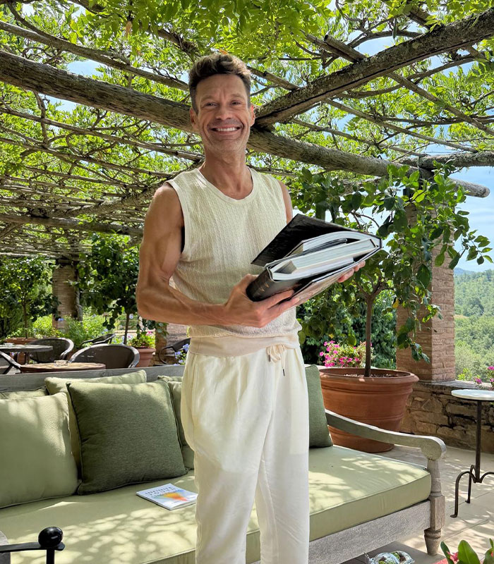 Ryan Seacrest smiling outdoors in sleeveless attire after his body transformation. Ryan Seacrest smiling outdoors in sleeveless attire after his body transformation.