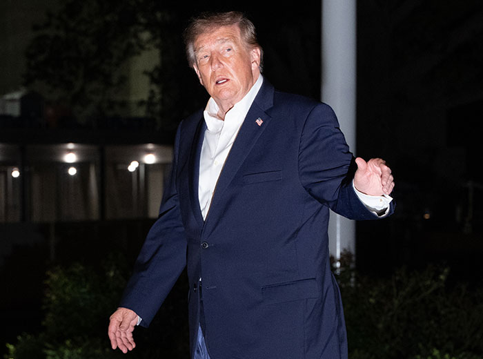 Donald Trump in a dark suit speaking at night on the White House grounds. Donald Trump in a dark suit speaking at night on the White House grounds.