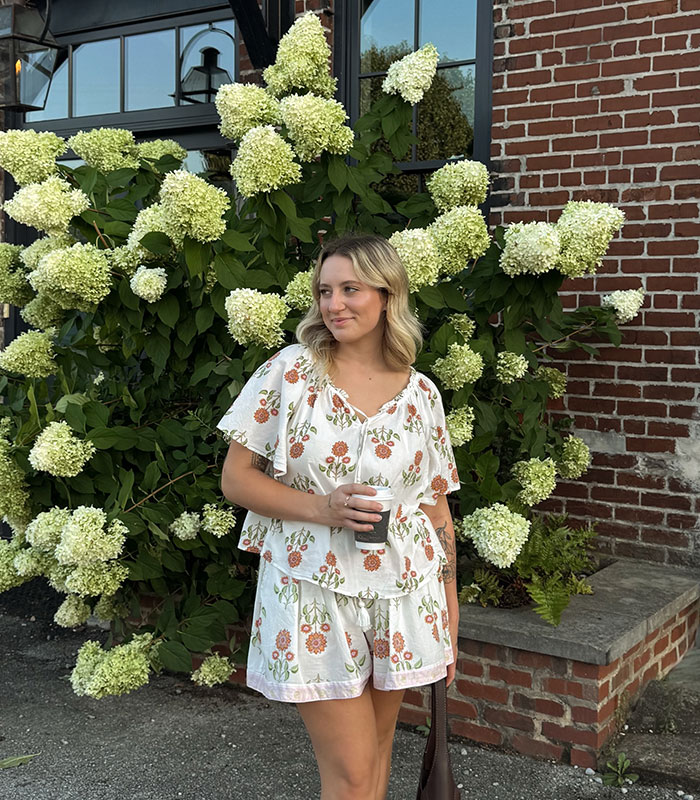 A blonde woman in a floral outfit holding a coffee cup, laughing at the marriage sacrifices drama