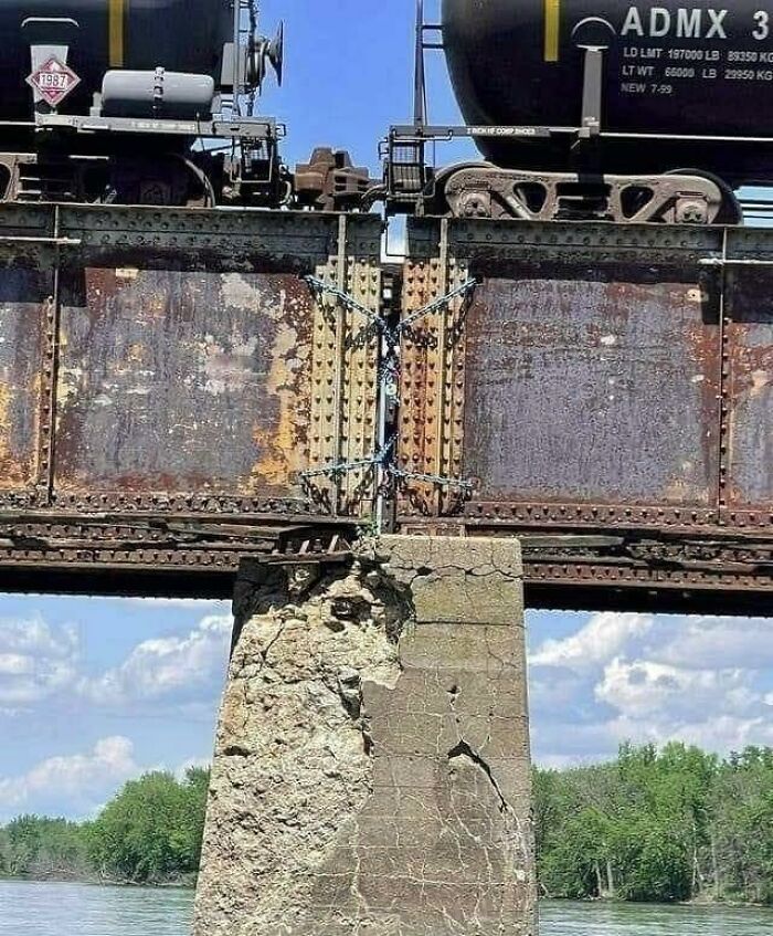 Rusty bridge held by chain brace and damaged concrete pillar