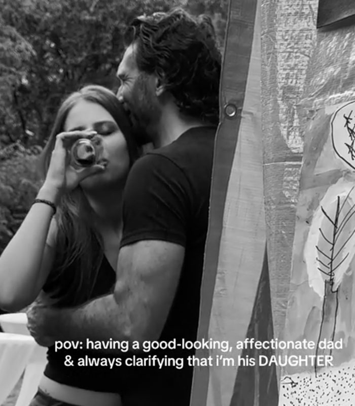 A black-and-white picture of a daughter holding a drink while sharing an embrace with her dad.