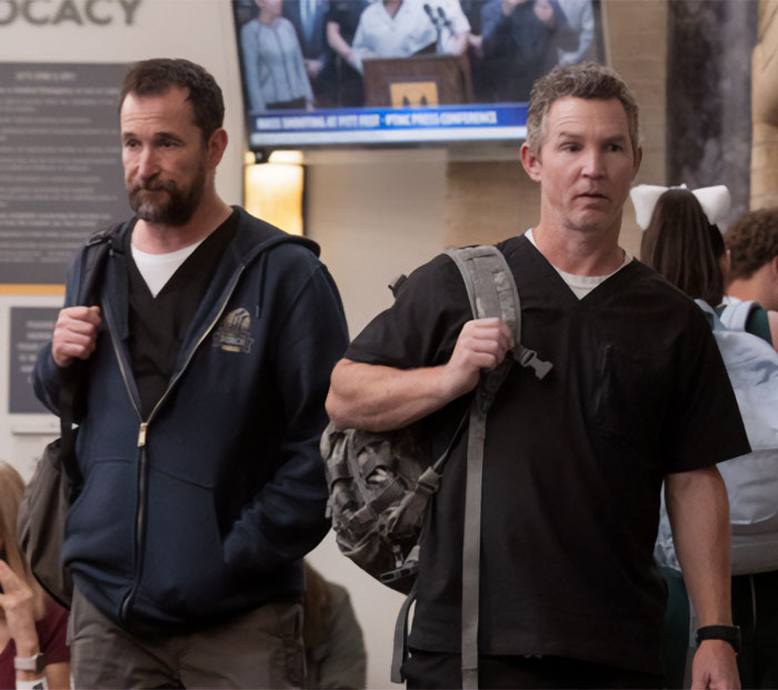 Noah Wyle carrying a backpack while walking alongside another actor on set