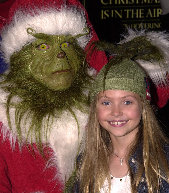 Young Taylor Momsen as Cindy Lou Who next to the Grinch in a festive costume.