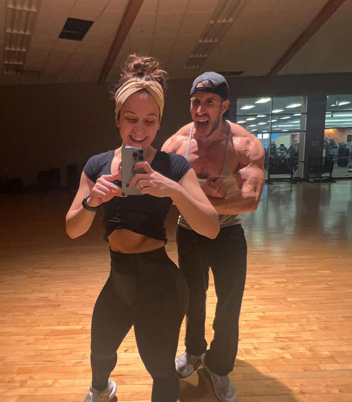 Disney World guest in athletic outfit taking a gym selfie with partner flexing behind her.