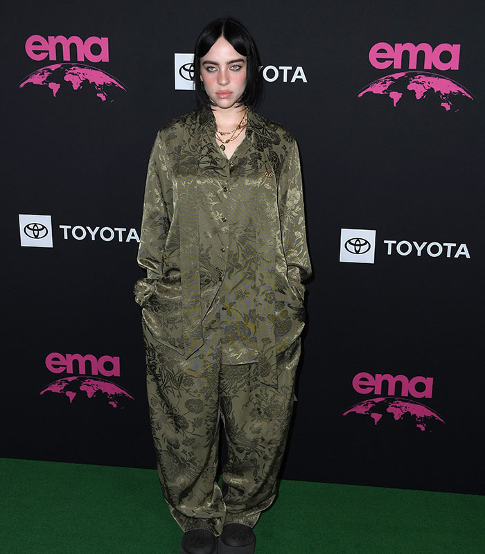 Billie Eilish posing at an event, displaying her slimmed down figure in a patterned green outfit Billie Eilish posing at an event, displaying her slimmed down figure in a patterned green outfit