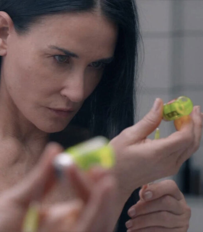 Demi Moore holds small yellow vials in a dramatic movie scene depicting beauty treatments and lip filler themes.