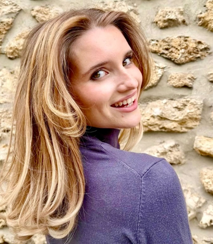 Portrait of an influencer with blonde hair smiling over her shoulder in a purple turtleneck sweater
