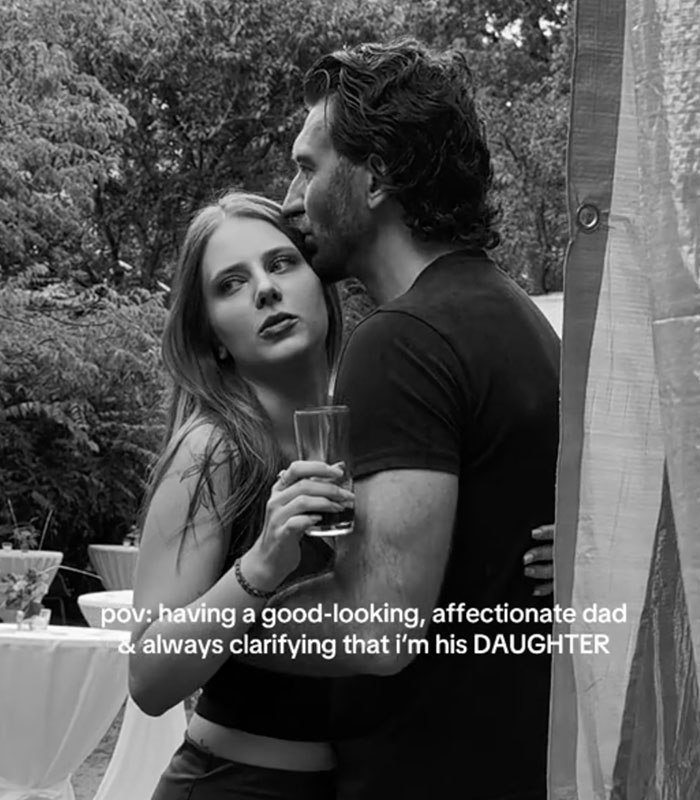 A black and white image of a young woman standing in a close bond with dad while holding a drink.