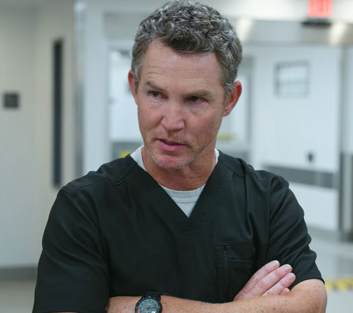 Actor wearing black scrubs with arms crossed looking concerned