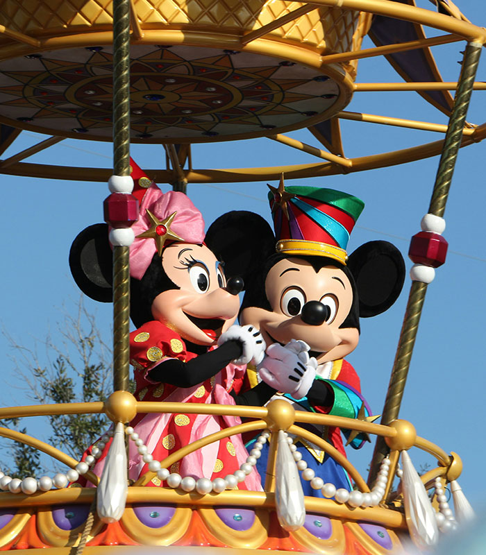 Mickey and Minnie Mouse waving during a parade at Disney World family park.