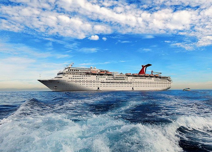 A white cruise ship sailing through deep blue ocean waters under a cloudy sky.