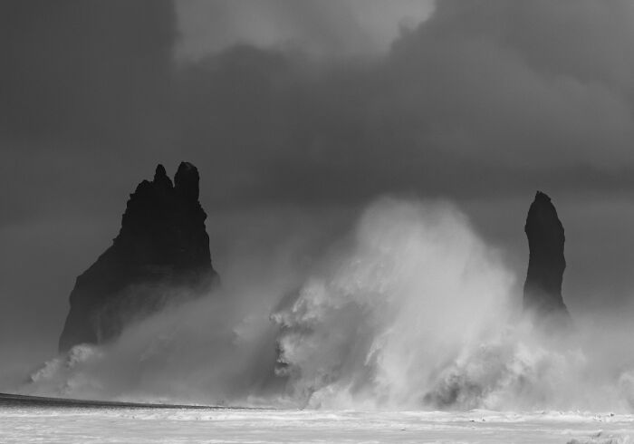 Massive waves crashing against rock stacks along a black sand coast in Iceland