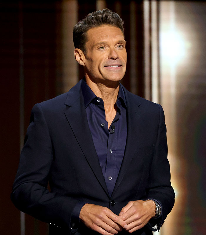 Ryan Seacrest hosting on stage in a dark blue suit, looking lean. Ryan Seacrest hosting on stage in a dark blue suit, looking lean.