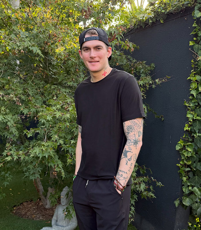 Cindy Crawford's son standing outside, showing tattoos and casual attire amid conversations of industry nepotism. Cindy Crawford's son standing outside, showing tattoos and casual attire amid conversations of industry nepotism.
