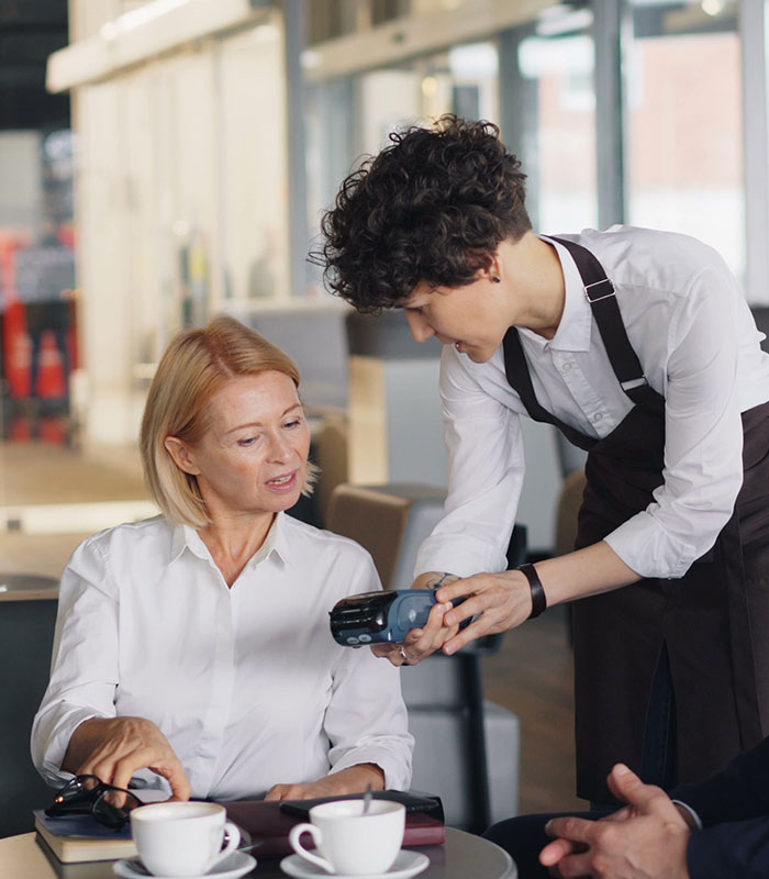 A server presenting a payment terminal to a customer at a cafe table. A server presenting a payment terminal to a customer at a cafe table.