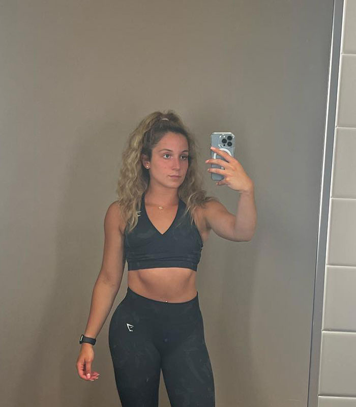 Woman in athletic crop top and leggings taking a mirror selfie, representing a Disney World guest.