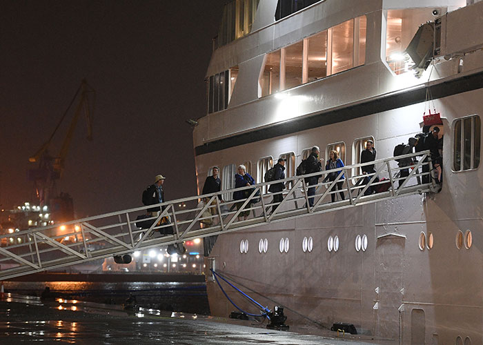 Passengers board a permanent cruise ship via gangway at night.