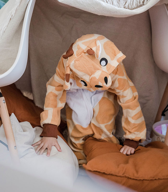 A young child playing indoors in a giraffe costume while home alone.