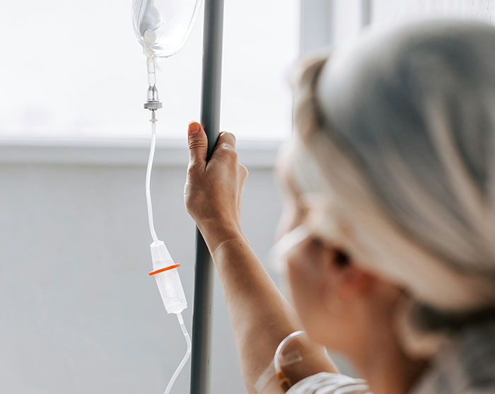 A cancer patient holding an IV drip stand while receiving medical treatment. A cancer patient holding an IV drip stand while receiving medical treatment.
