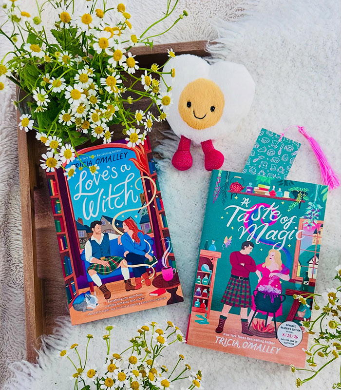 Two romantasy books with colourful covers surrounded by white flowers on a wooden tray
