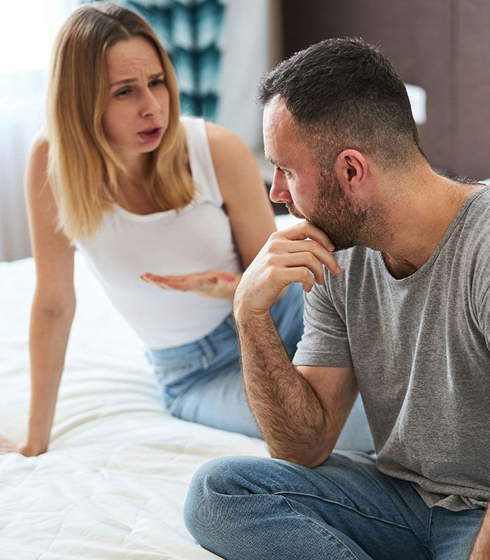 An angry woman confronting a man hiding secrets while sitting on a bed An angry woman confronting a man hiding secrets while sitting on a bed
