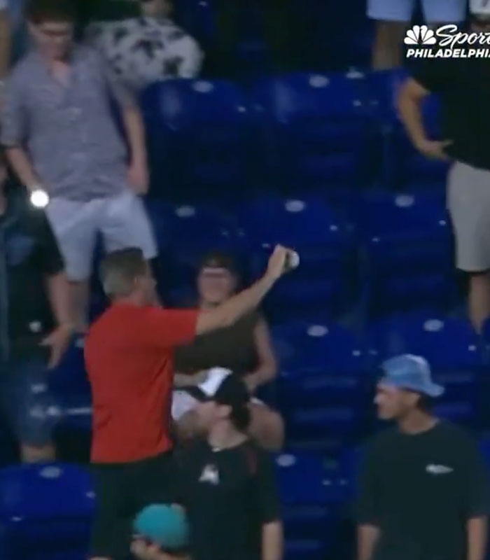 An adult fan holds up a baseball in the stadium stands, refusing to hand over his ball to a young fan.