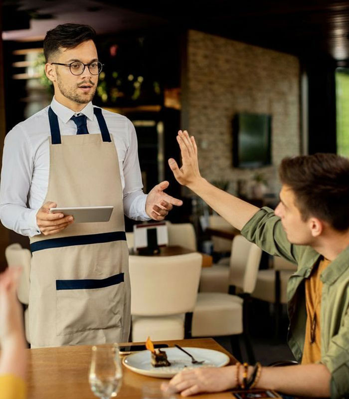 A restaurant customer making a hand gesture while a server holding a tablet listens. A restaurant customer making a hand gesture while a server holding a tablet listens.