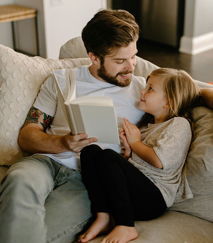 A father reading a book to his young daughter, showing a healthy bond with dad.