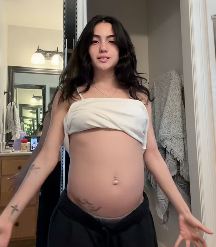 A woman showing her bloated belly in a mirror before her transformation journey. A woman showing her bloated belly in a mirror before her transformation journey.