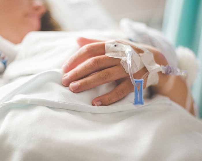A patient lying in a hospital bed with an IV line attached to their hand, highlighting rising cancer rates. A patient lying in a hospital bed with an IV line attached to their hand, highlighting rising cancer rates.